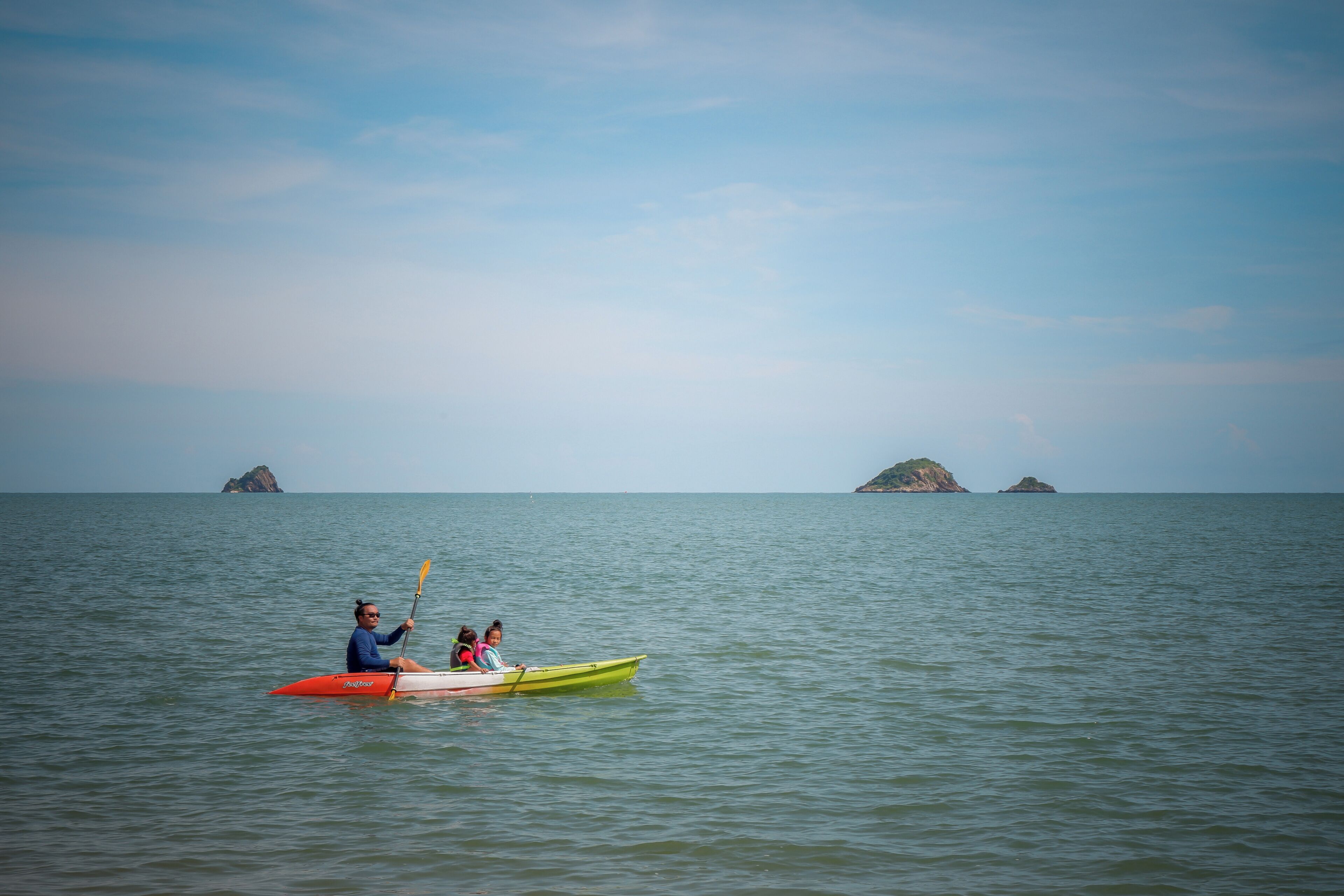 A calm sea with two kayaks, one red and one green, with a person paddling the red kayak.