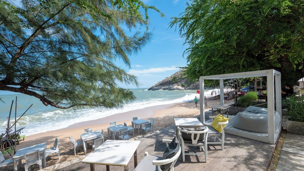 Un espace extérieur aménagé avec des tables et des chaises, offrant une vue sur une plage et l’océan.