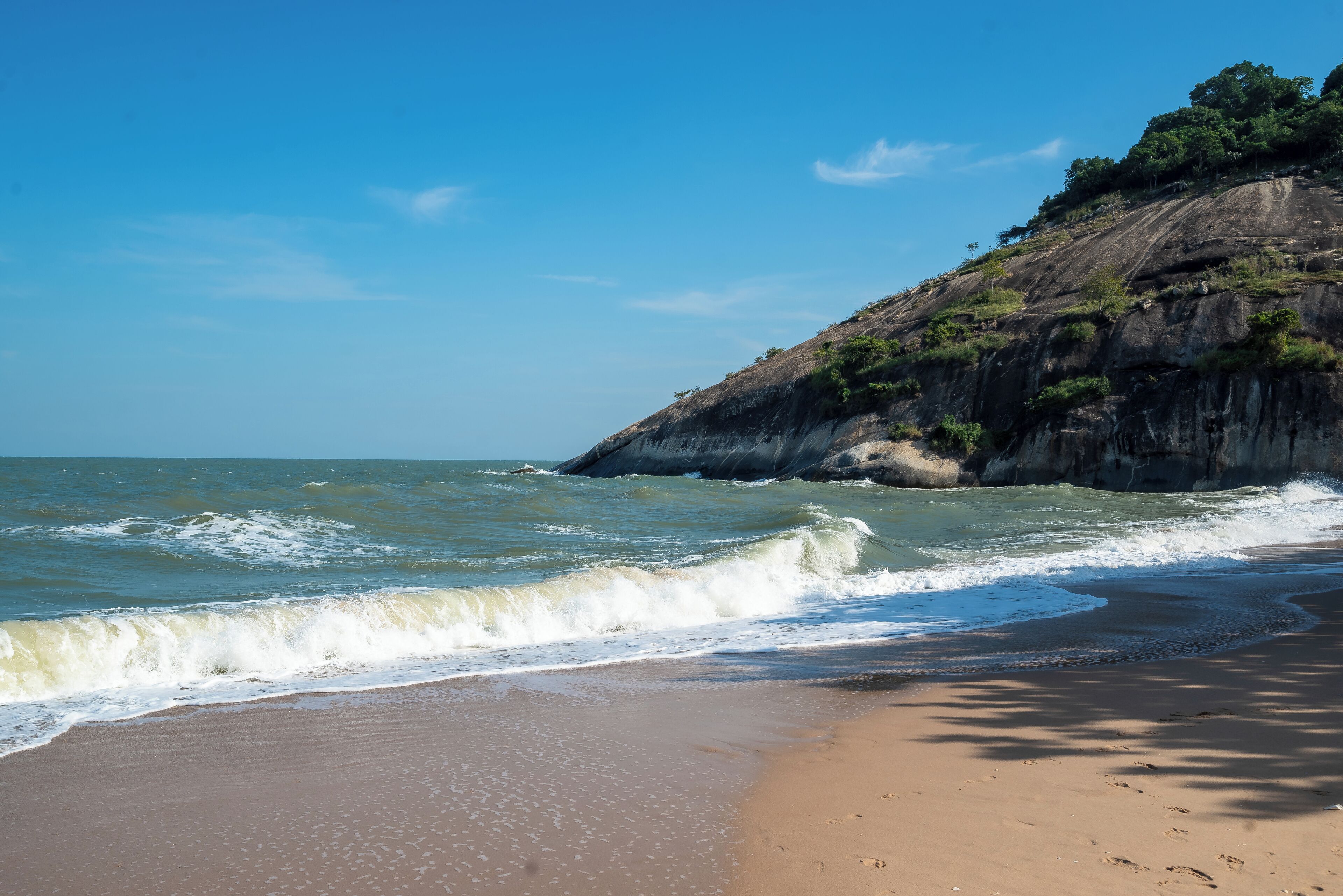 A beach with waves, a sandy shore, and a rocky cliff with vegetation.
