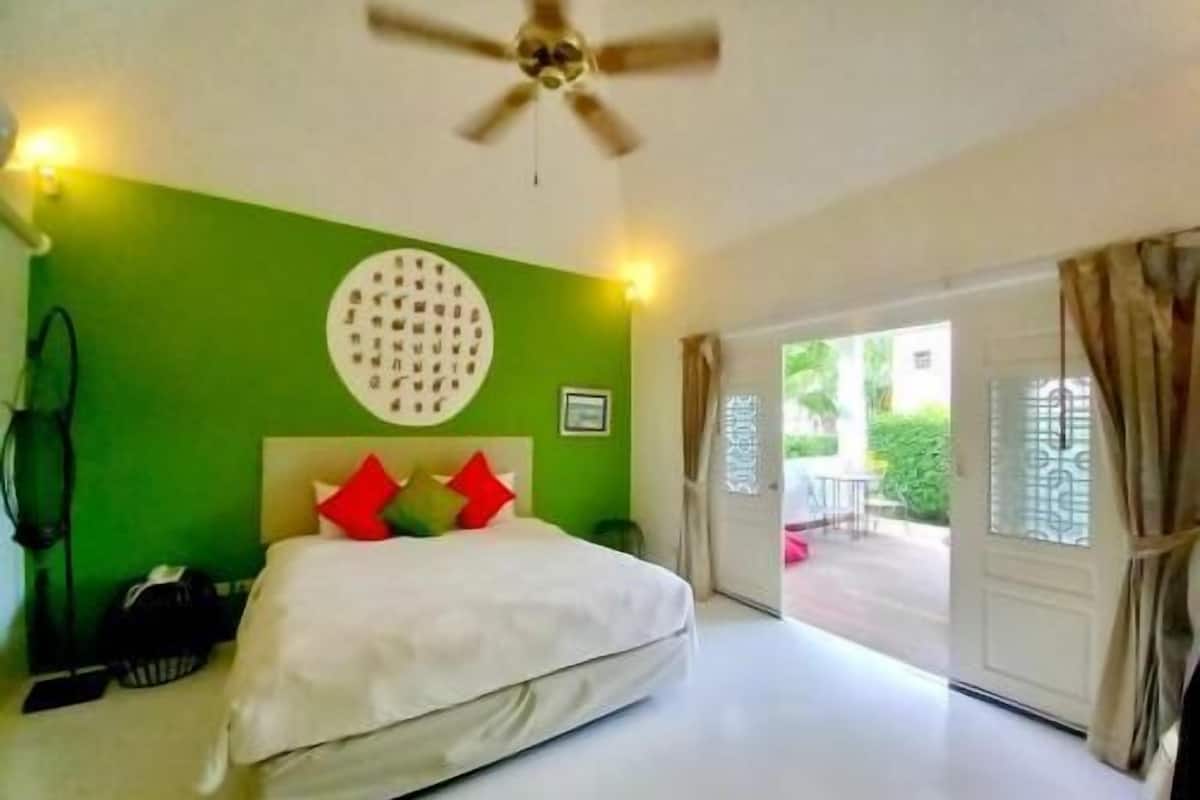 Ein Schlafzimmer mit einem Bett, einem Deckenventilator, einer grünen Wand und Blick durch die Tür.
