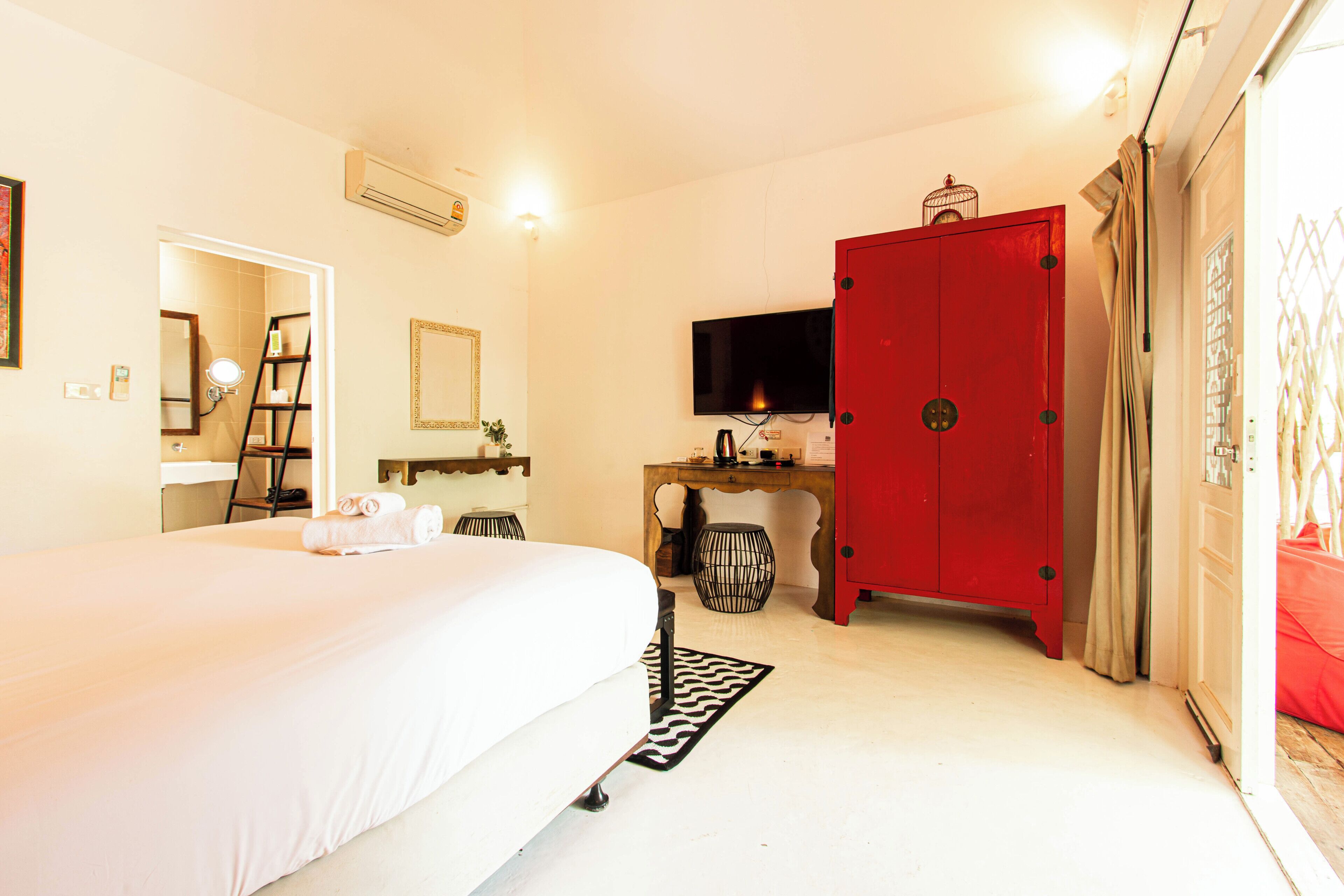 Una habitación de hotel con una cama, un escritorio con televisor, un armario rojo y un espejo.