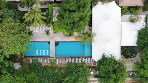 Vue aérienne d’un complexe hôtelier avec des bâtiments aux toits de chaume, une piscine centrale et une végétation luxuriante.