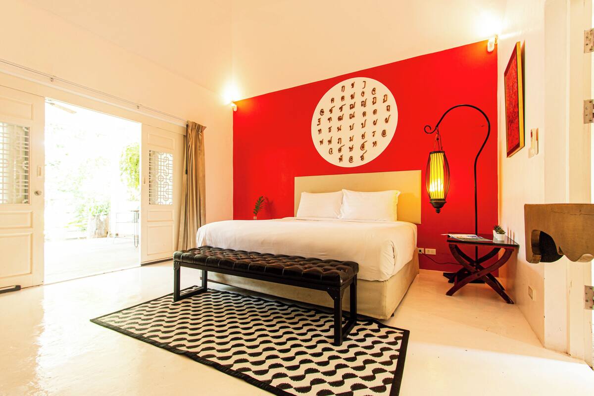 Ein Schlafzimmer mit Bett, einer Bank, einer runden Wanddekoration, einem Nachttisch und einer Lampe.