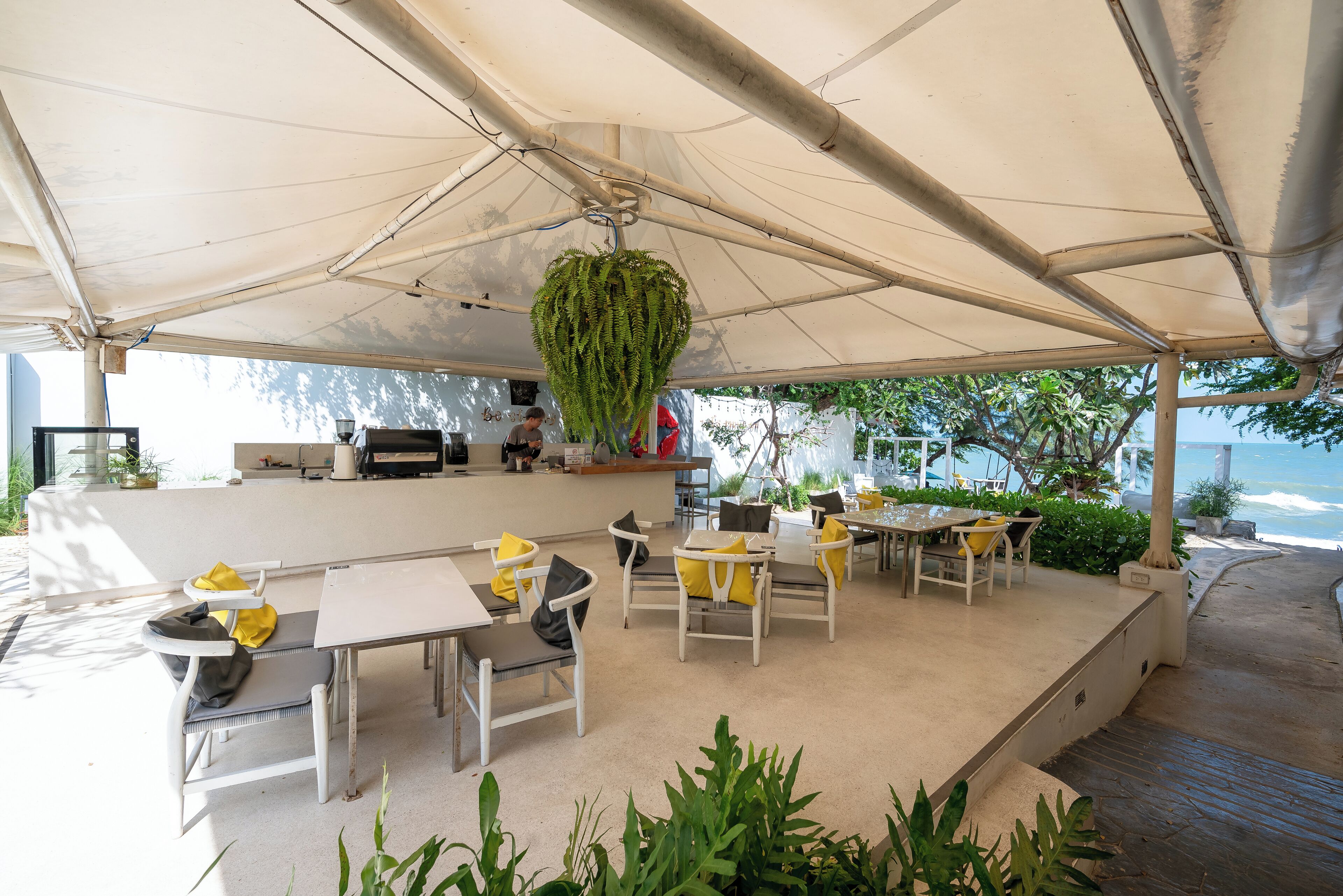 An outdoor seating area with white tables and chairs, a hanging plant, and a view of the ocean.