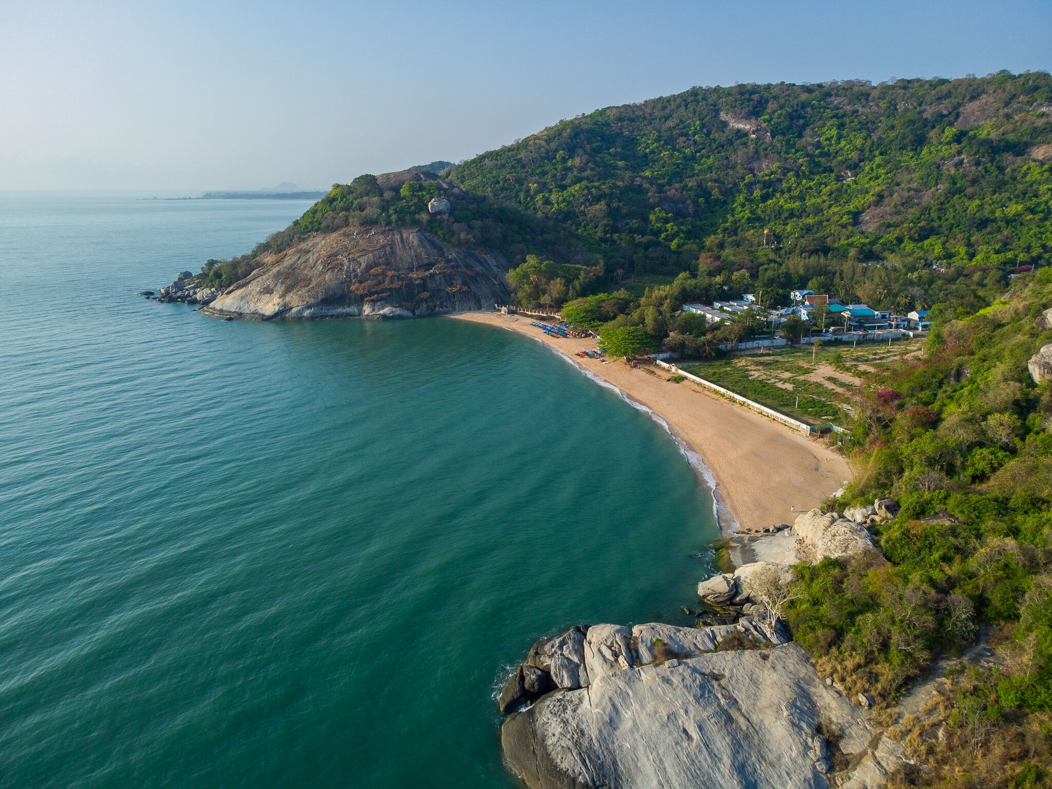 A coastal landscape with a beach, rocky cliffs, and a hillside with buildings.