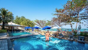 Une piscine dont le sol est recouvert de carrelage, avec des chaises longues et des parasols.