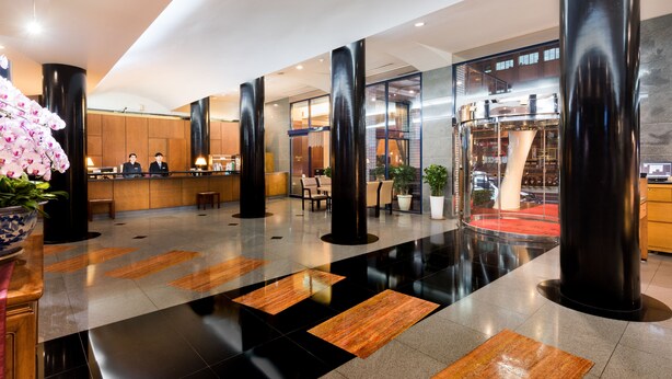 A modern hotel lobby with a reception desk, seating area, and a staircase leading to an upper floor. - Hotel Tainan (Tainan)