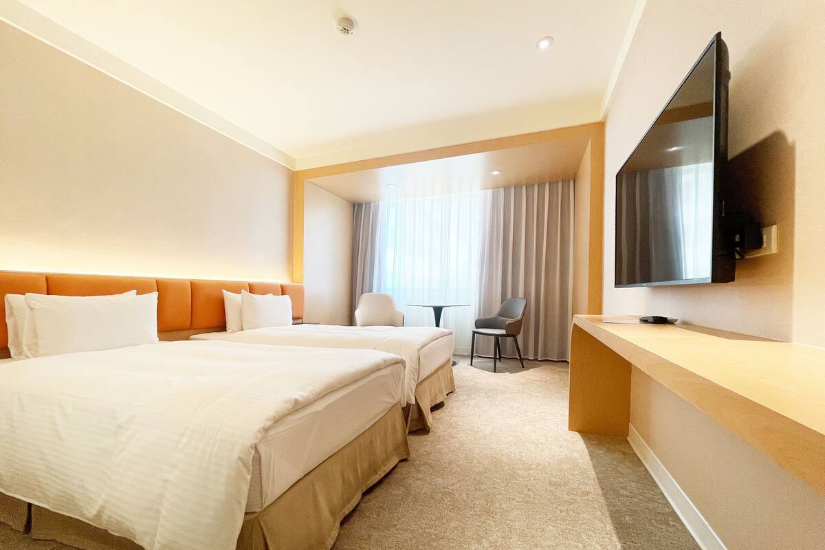 Ein Hotelzimmer mit zwei Betten, einem Fernseher, einem Schreibtisch und einem Sessel.