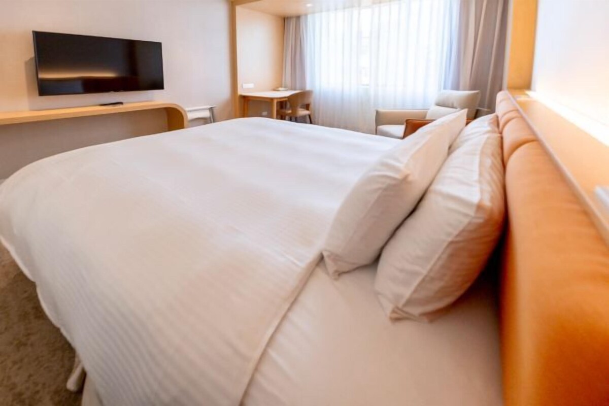 A hotel room with a large bed, a flat-screen TV mounted on the wall, a desk, and a chair.