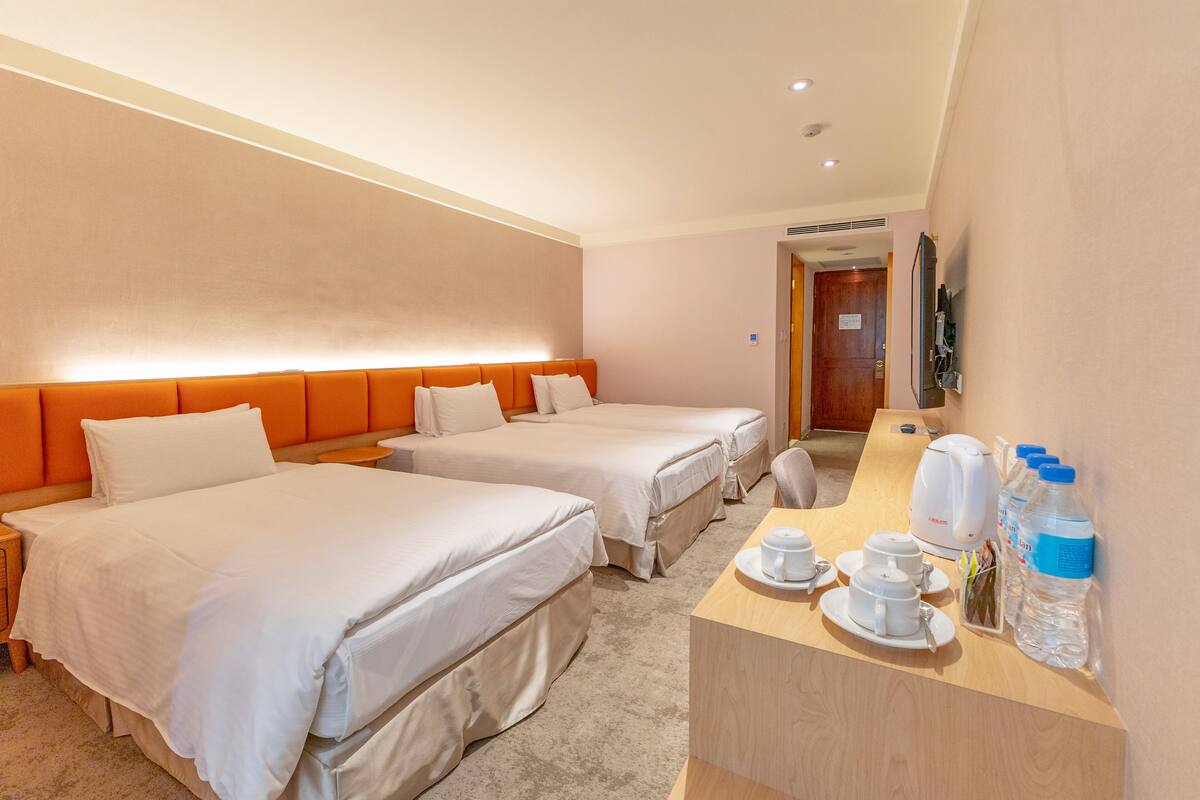 Ein Hotelzimmer mit zwei Betten, einem Holztisch mit Wasserkocher, Tassen und Wasserflaschen.