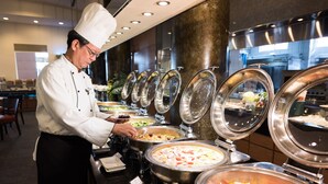 A buffet setup with multiple food stations, a chef serving food, and a modern interior design. - Hotel Tainan (Tainan)
