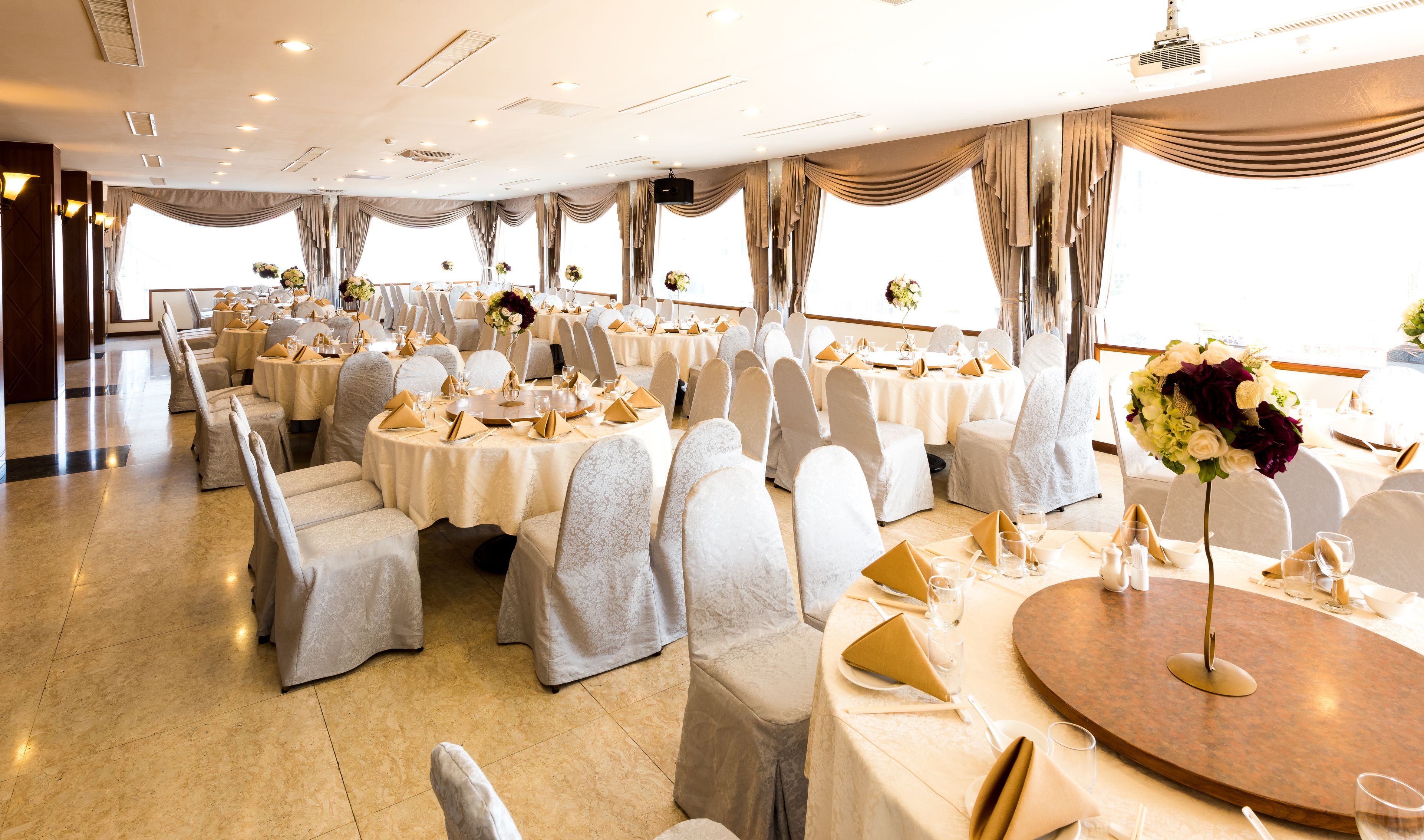 A banquet hall with round tables, white chairs, and chandeliers.
