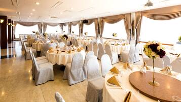 A banquet hall with round tables, white chairs, and chandeliers.