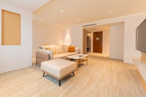 A modern living room with a sofa, ottoman, and coffee table, a flat-screen TV, and a wooden door leading to another room. - Hotel Tainan (Tainan)