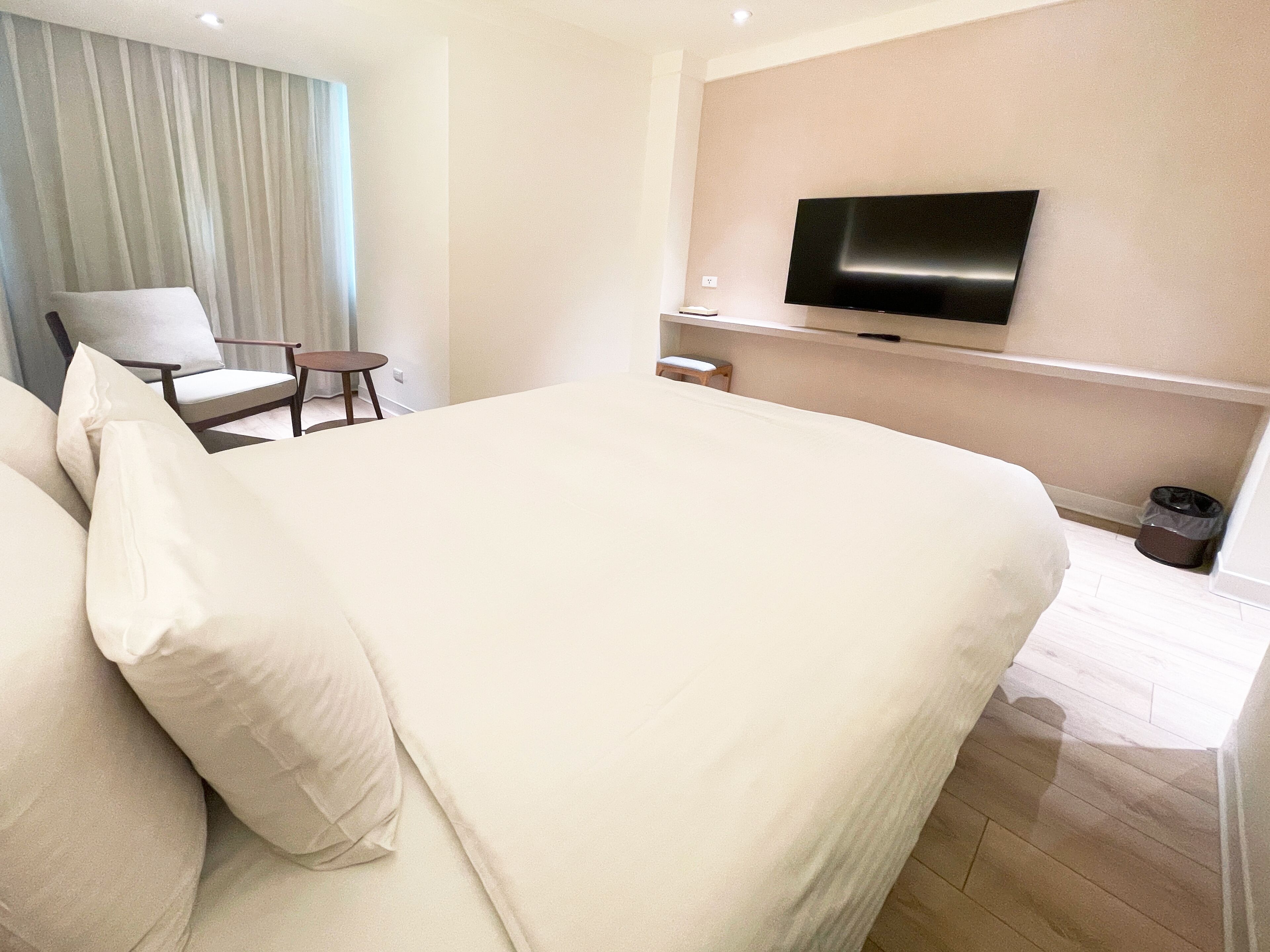 A hotel room with a large bed, a TV mounted on the wall, a chair, and a small table.