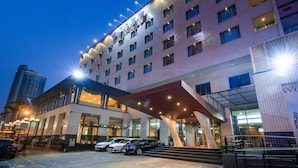 A multi-story hotel with a modern design, featuring a prominent entrance with a covered area and a parking lot with several cars. - Hotel Tainan (Tainan)
