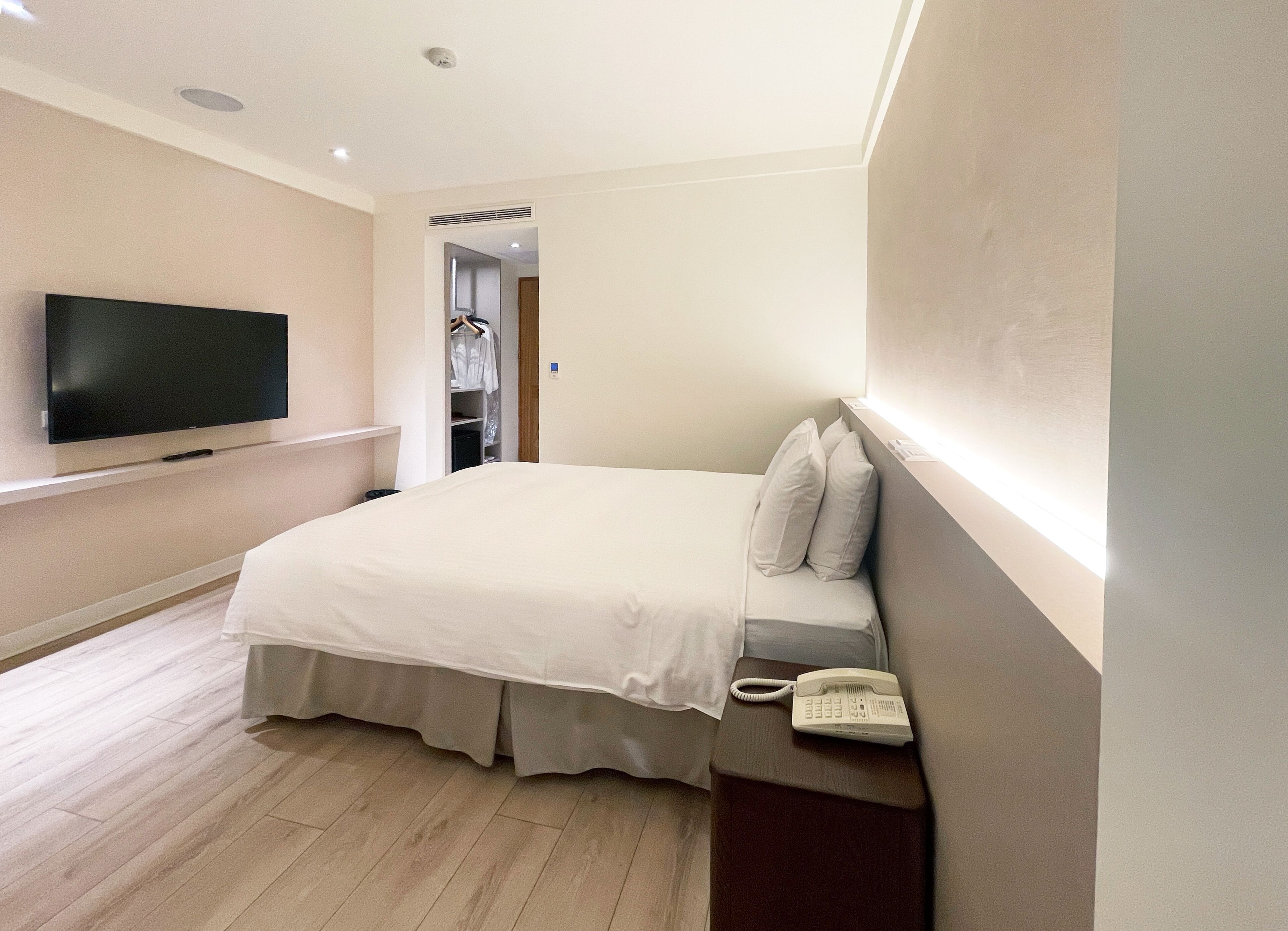 A hotel room with a bed, a bedside telephone, a television mounted on the wall, and a wooden floor.