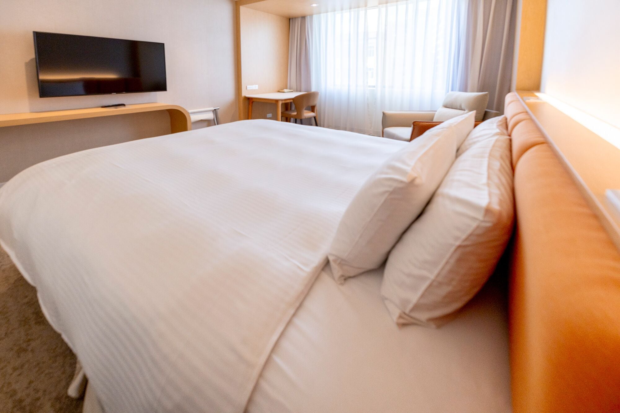A hotel room with a large bed, a flat-screen TV mounted on the wall, a desk, and a chair.