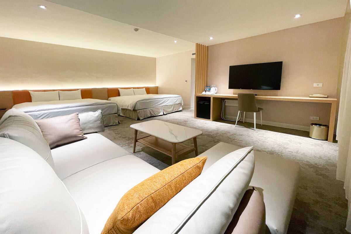 Ein modernes Hotelzimmer mit einer großen Couch, einem kleinen Sofa, einem Couchtisch und einem an der Wand montierten Flachbildfernseher.