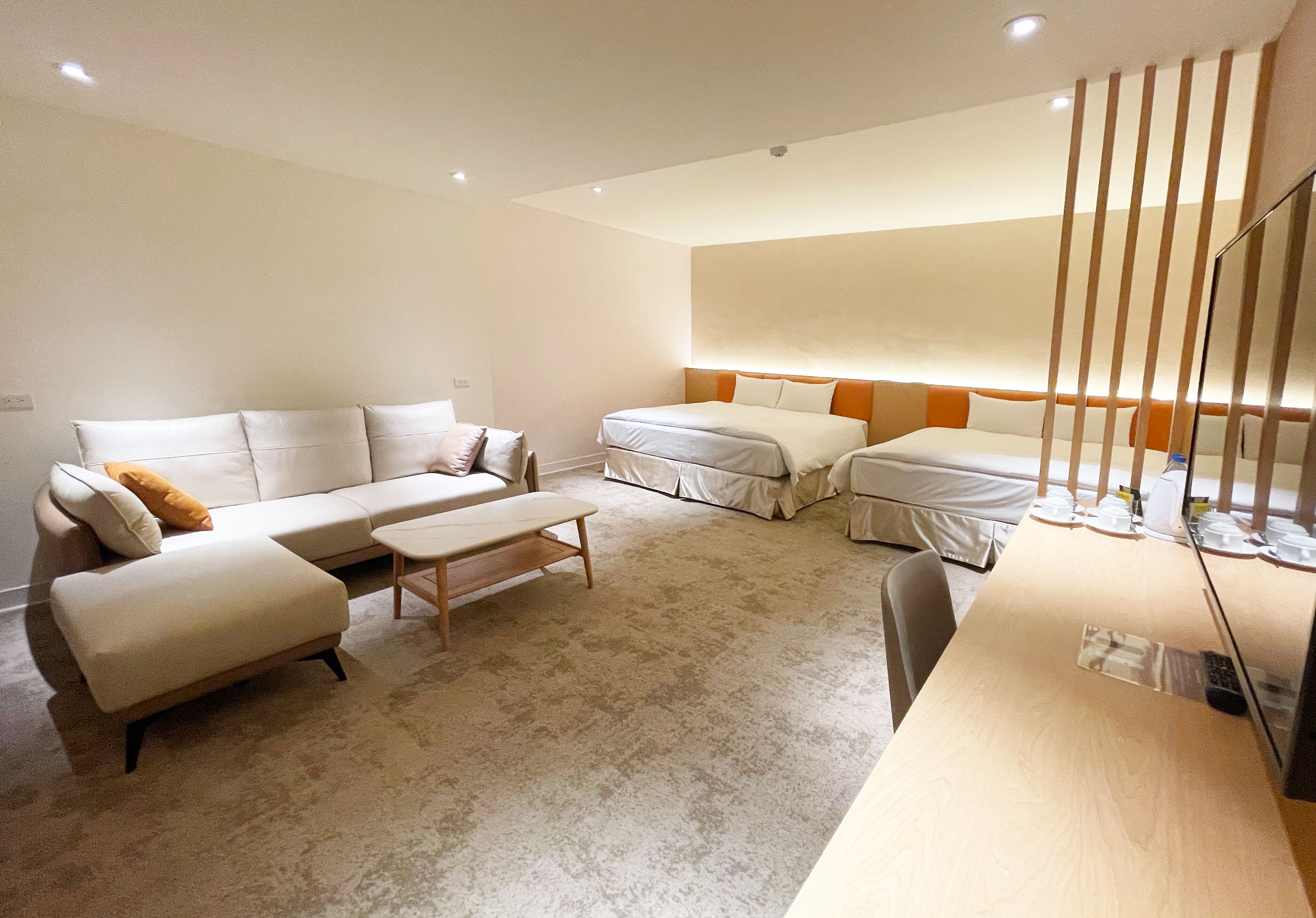 Une chambre d’hôtel moderne avec un canapé, deux lits, un bureau en bois et un grand miroir.