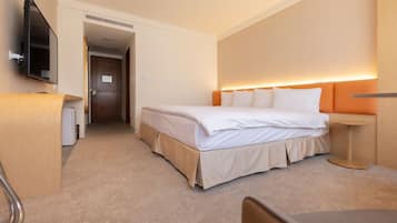Habitación de hotel con cama, televisor montado en la pared, escritorio y una silla.
