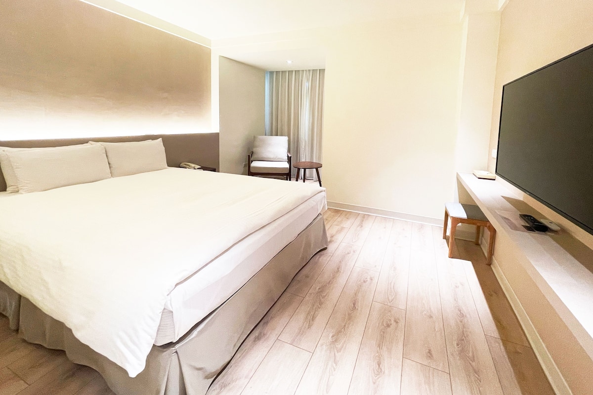 Ein Hotelzimmer mit einem großen Bett, einem Sessel, einem Fernseher und einem kleinen Tisch.
