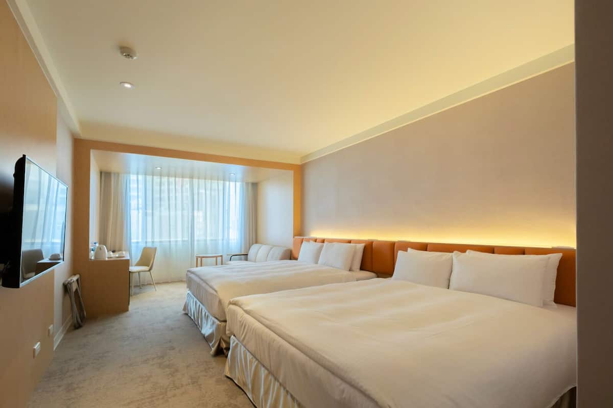 Ein Hotelzimmer mit zwei Betten, einem Fernseher, einem Schreibtisch und einem Sessel.