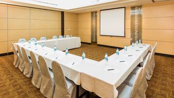 A conference room with a long table, chairs, water bottles, and a projector screen.