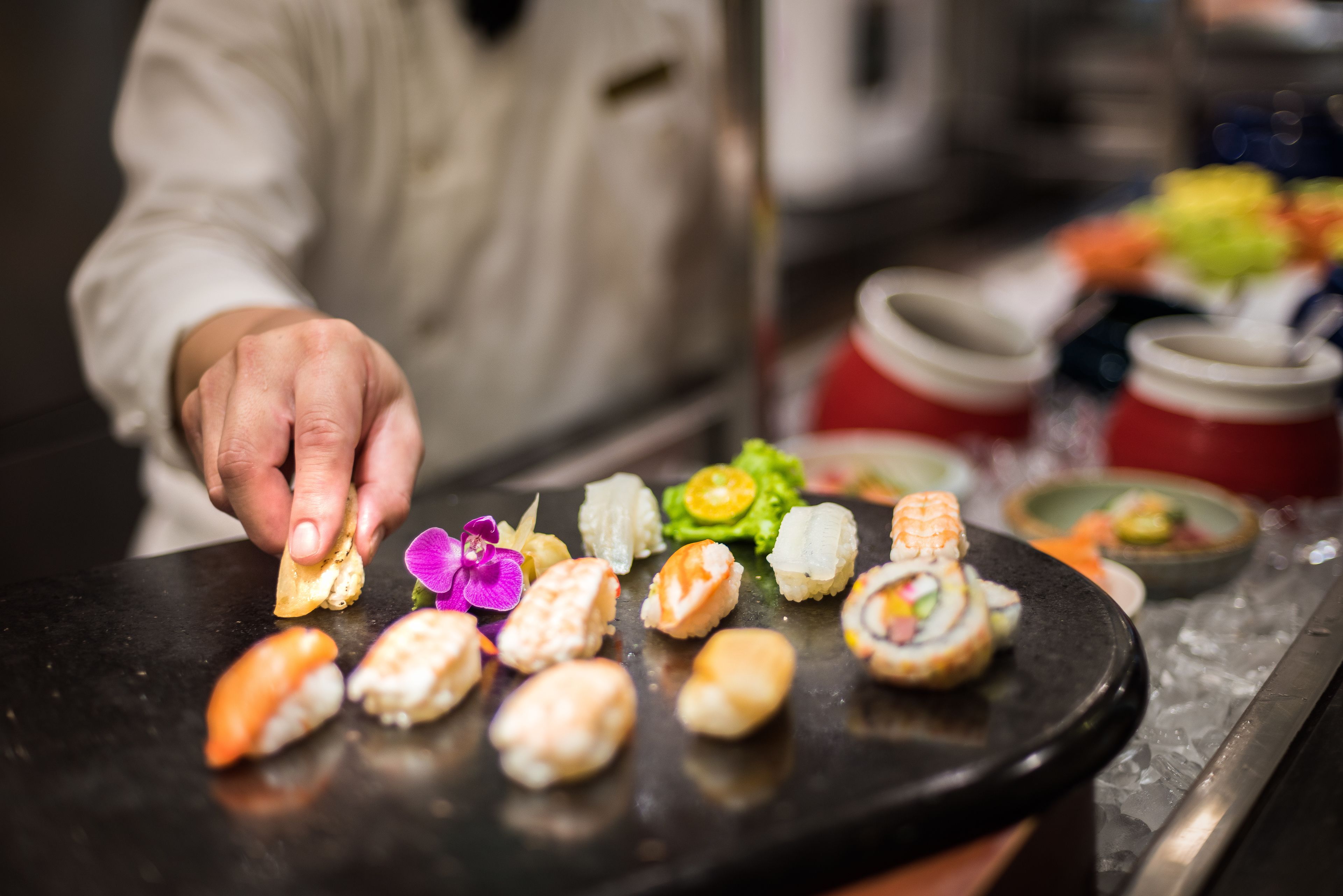 A sushi platter with various types of sushi and a hand picking one.