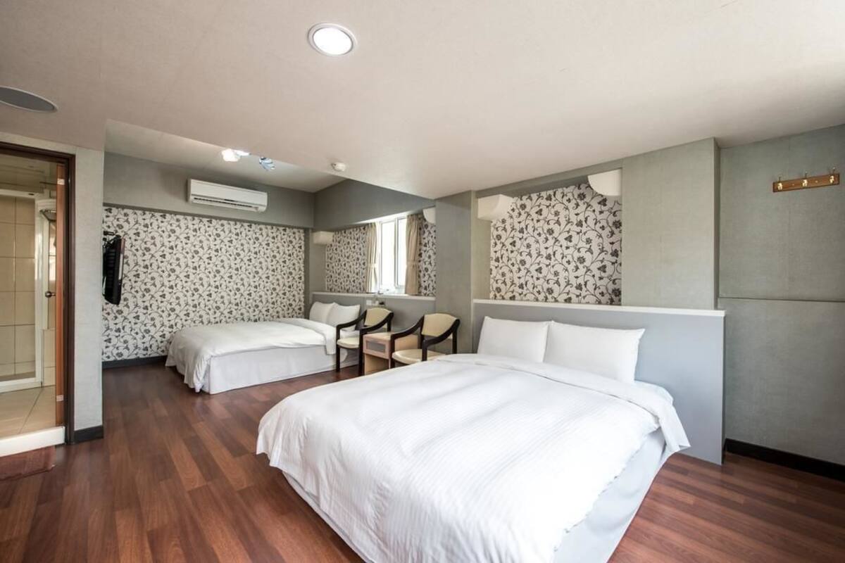 A hotel room with two beds, a sitting area with chairs, a large mirror, and a shower area.