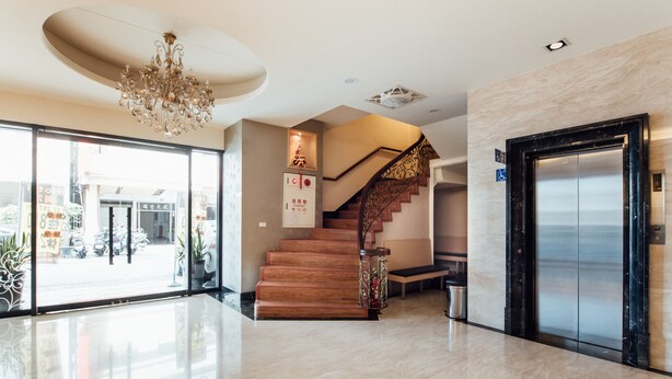 A modern lobby with a marble floor, a wooden staircase, and a large elevator.