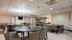 A modern dining area with round tables and chairs, a chandelier, and a flat-screen TV mounted on the wall.