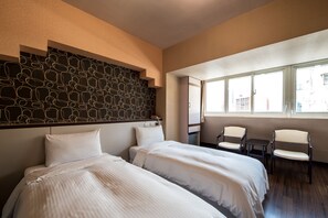 A hotel room with two beds, a seating area with chairs, a patterned wall, and a window with a view of buildings. - Hotel South Sea (Kaohsiung)