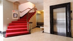 A hotel lobby with a red carpeted staircase, an elevator, and a marble floor.