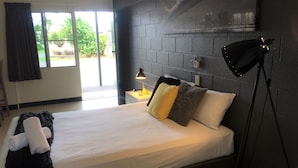 A modern hotel room with a large bed, a nightstand, a lamp, and a view of the outdoors.
