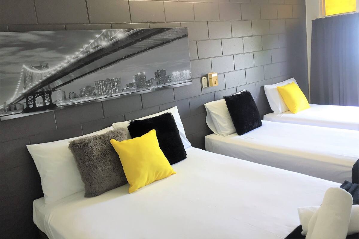 A hotel room with two beds, each with white bedding and yellow and black pillows. A large cityscape mural is on the wall behind the beds.