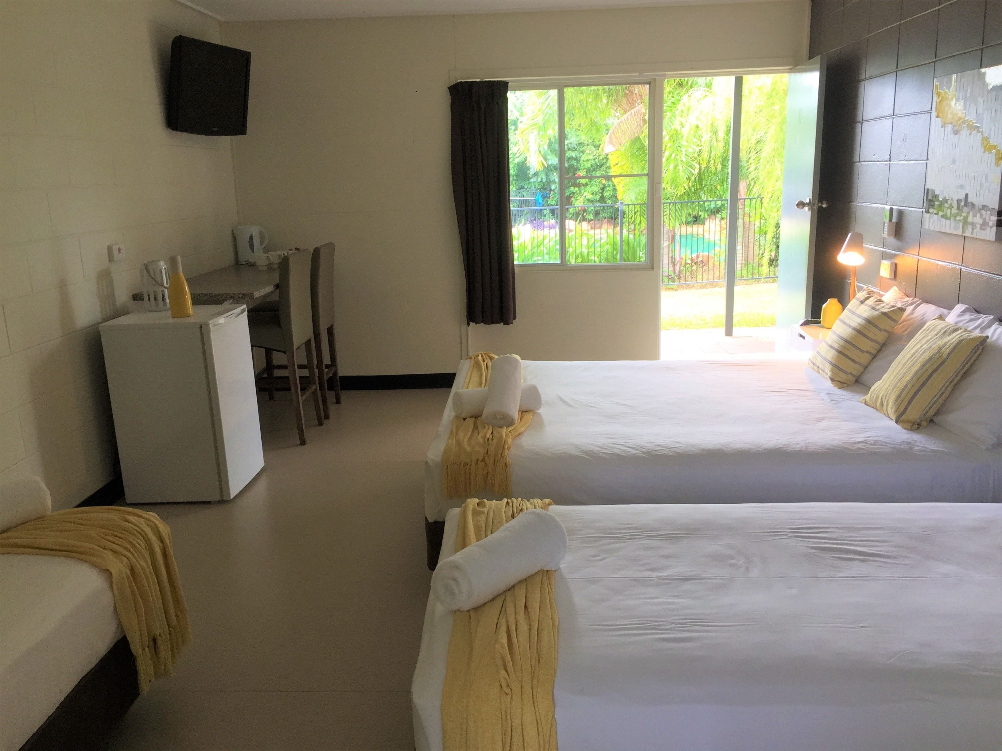 A hotel room with two beds, a desk, a refrigerator, and a TV on the wall.