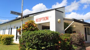 A reception area with a sign, a building with a white exterior, and some greenery in front.