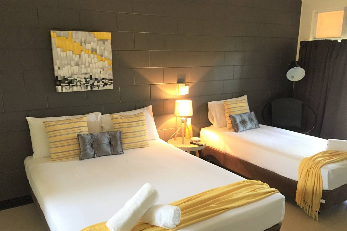 A hotel room with two beds, a nightstand with a lamp, a painting on the wall, and a window with curtains.
