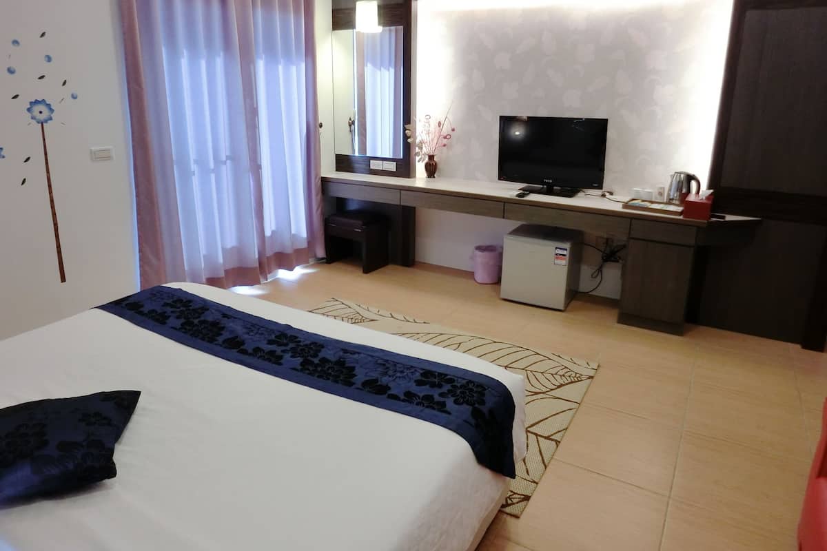 Habitación de hotel con cama, escritorio, televisor y un refrigerador pequeño.