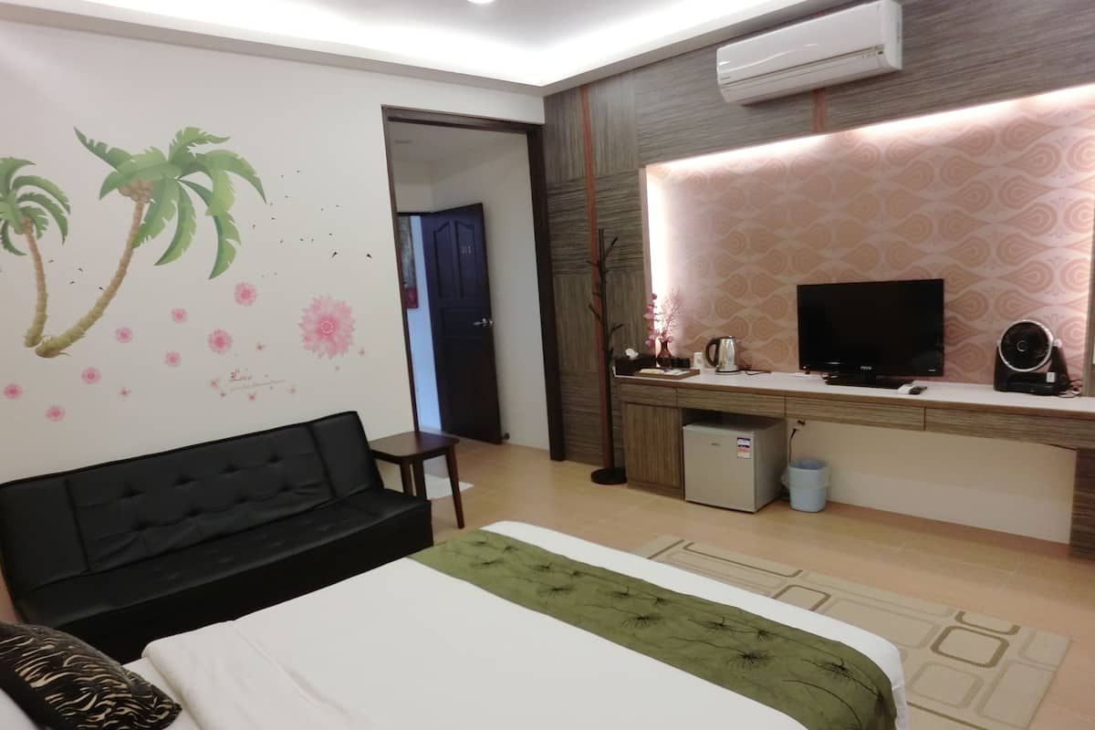 Una habitación de hotel con una cama, un sofá negro, un escritorio con televisor y aire acondicionado.