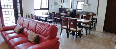 A spacious living area with a red leather sofa, dining table, and chairs.