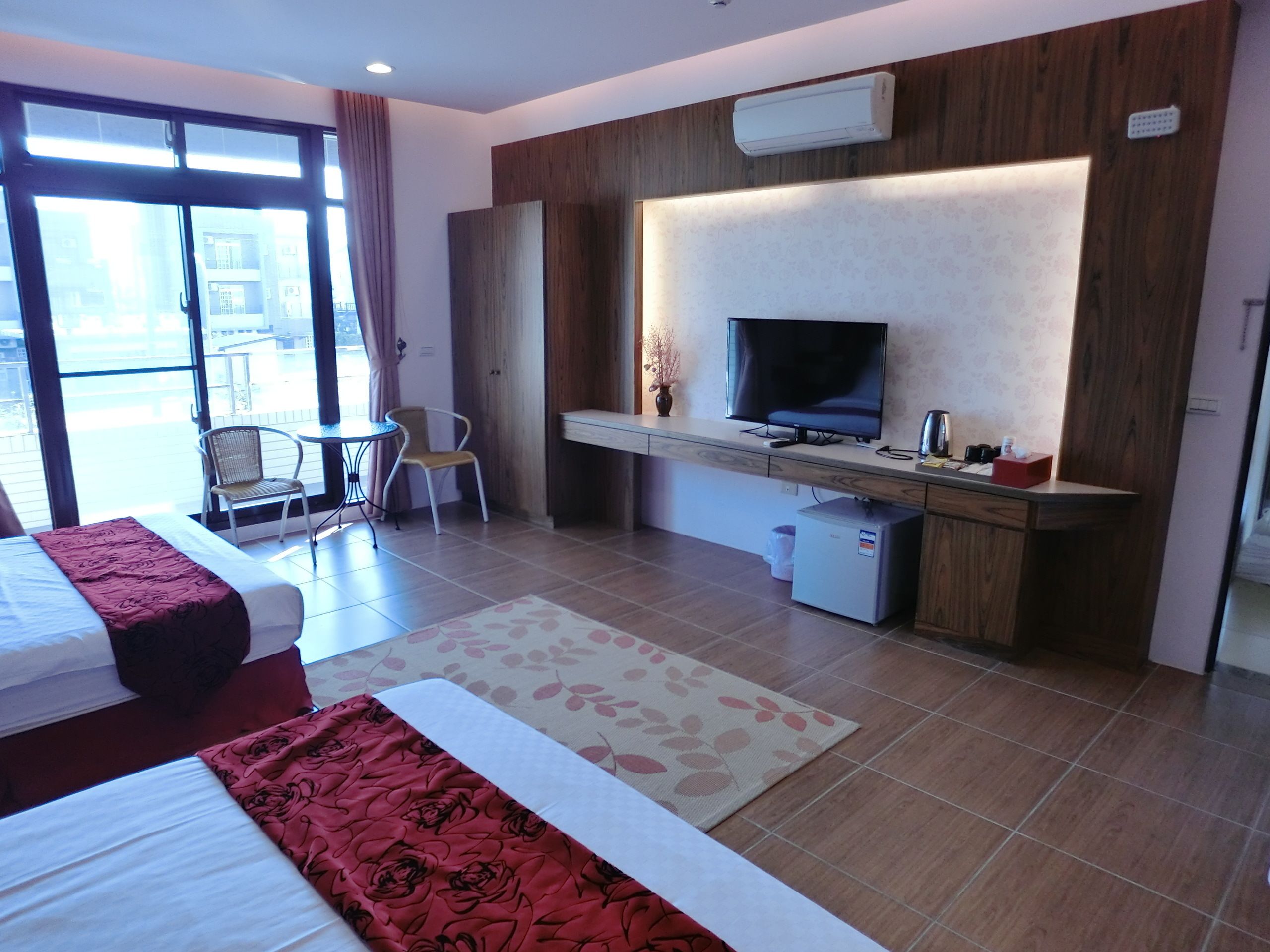 A hotel room with a bed, a desk with a TV, a small fridge, and a chair.