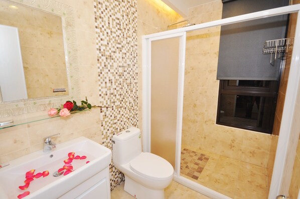 Une salle de bain avec une douche à parois de verre, des toilettes et un lavabo décoré de pétales de rose.