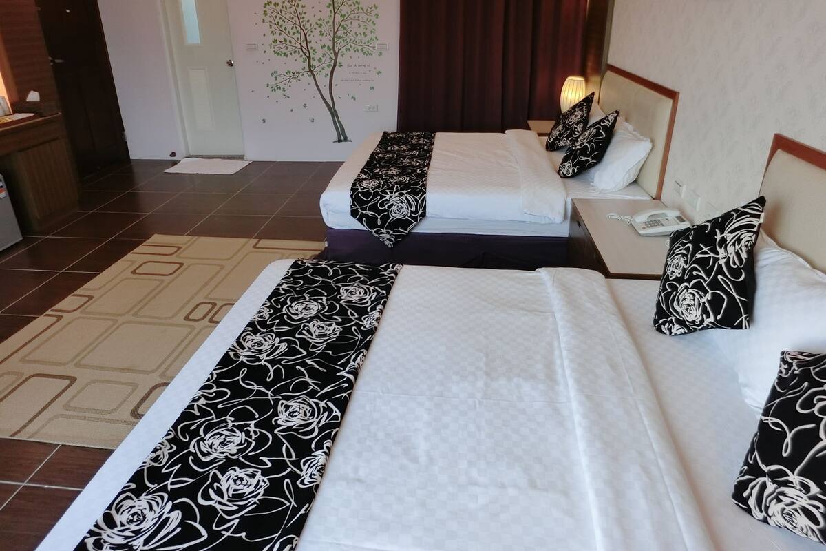 Habitación de hotel con dos camas, cada una con colchas y almohadas estampadas en blanco y negro. Hay una mesita con una lámpara y un teléfono.