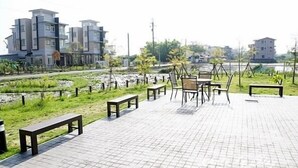 A paved outdoor area with benches and chairs, a small water body, and buildings in the background. - Love Play House (Luodong)