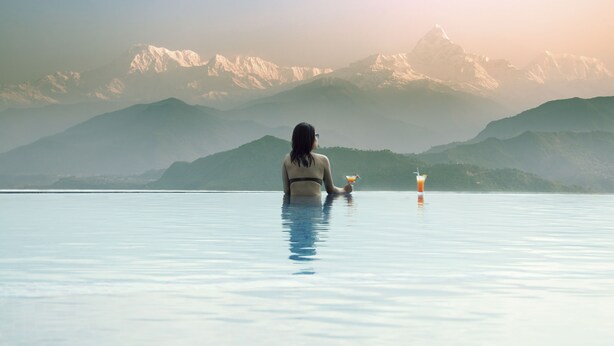 A person sitting in a large, clear pool with a mountain view in the background. - Himalayan Front Hotel by KGH Group (Pokhara)