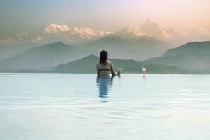 A person sitting in a large, clear pool with a mountain view in the background.