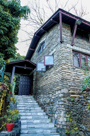 A stone house with a wooden staircase leading to the entrance, surrounded by greenery. - Himalayan Front Hotel by KGH Group (Pokhara)