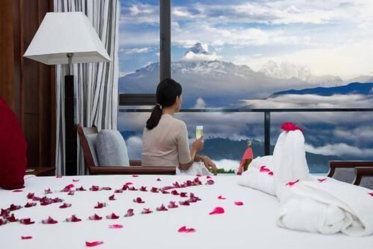 A room with a bed, a window with a mountain view, and a lamp.